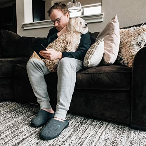 Man sitting on couch reading with dog on lap.