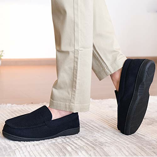 Man wearing black loafers and beige pants on a carpeted floor.